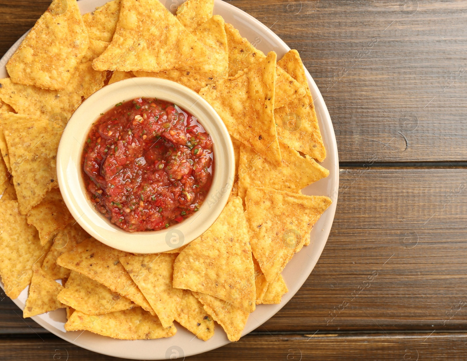 Photo of Delicious salsa with nachos on wooden table, top view