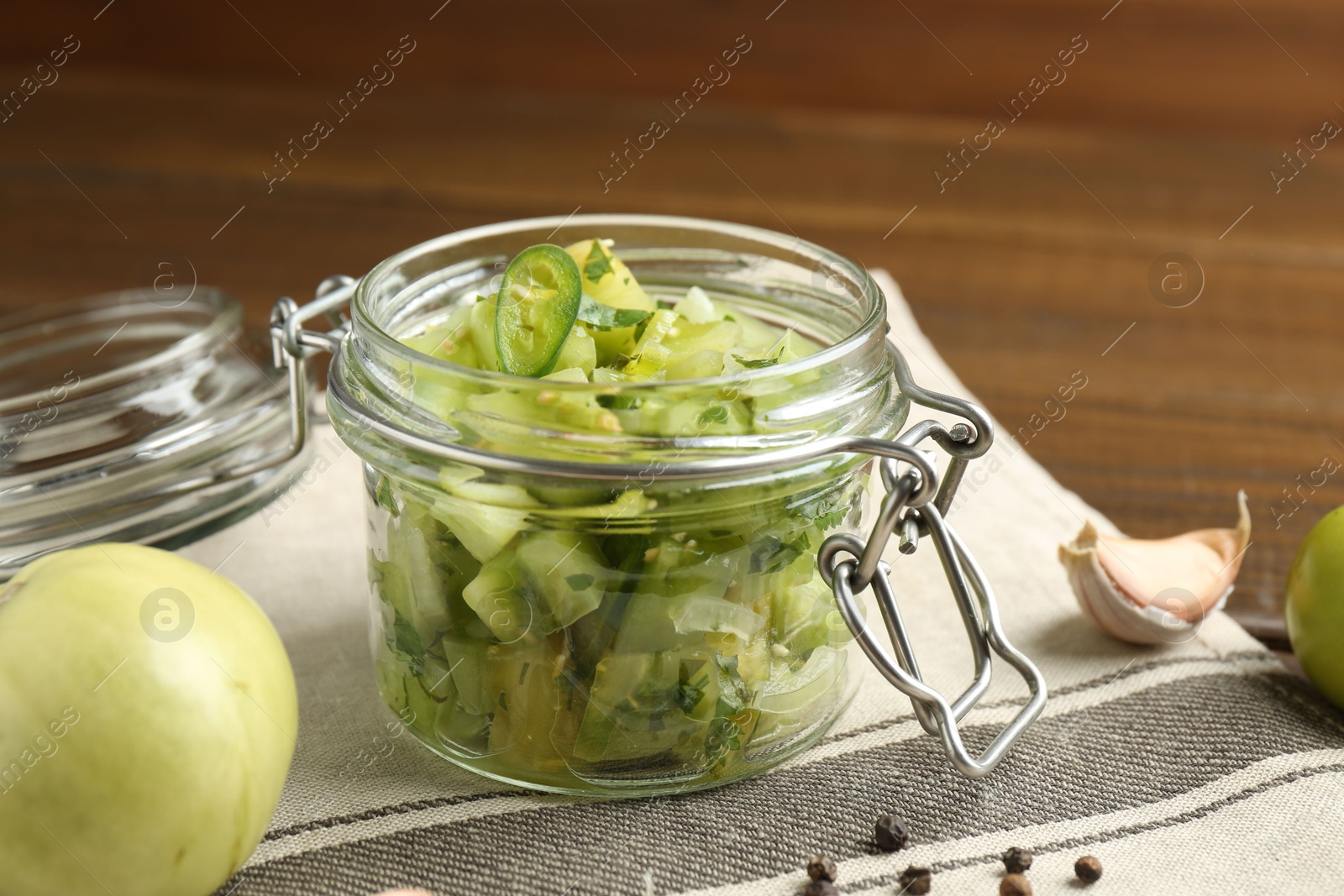 Photo of Delicious green salsa in jar and ingredients on wooden table, closeup