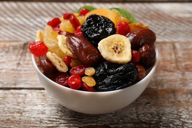 Photo of Mix of different dried fruits in bowl on wooden table, closeup