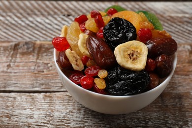 Photo of Mix of different dried fruits in bowl on wooden table, closeup