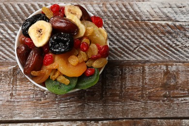 Photo of Mix of different dried fruits in bowl on wooden table, top view. Space for text