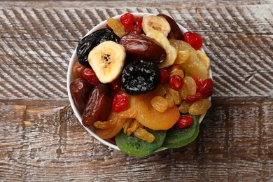 Photo of Mix of different dried fruits in bowl on wooden table, top view