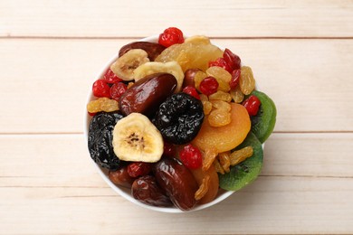 Photo of Mix of different dried fruits in bowl on white wooden table, top view