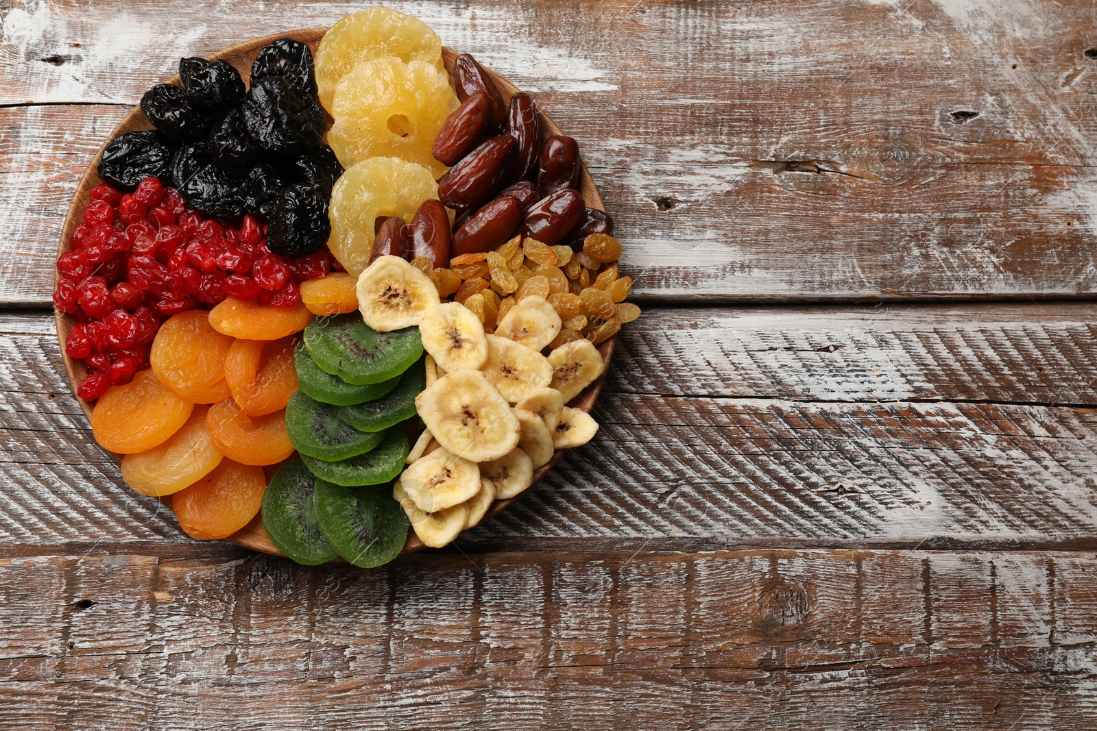 Photo of Different dried fruits on wooden table, top view. Space for text