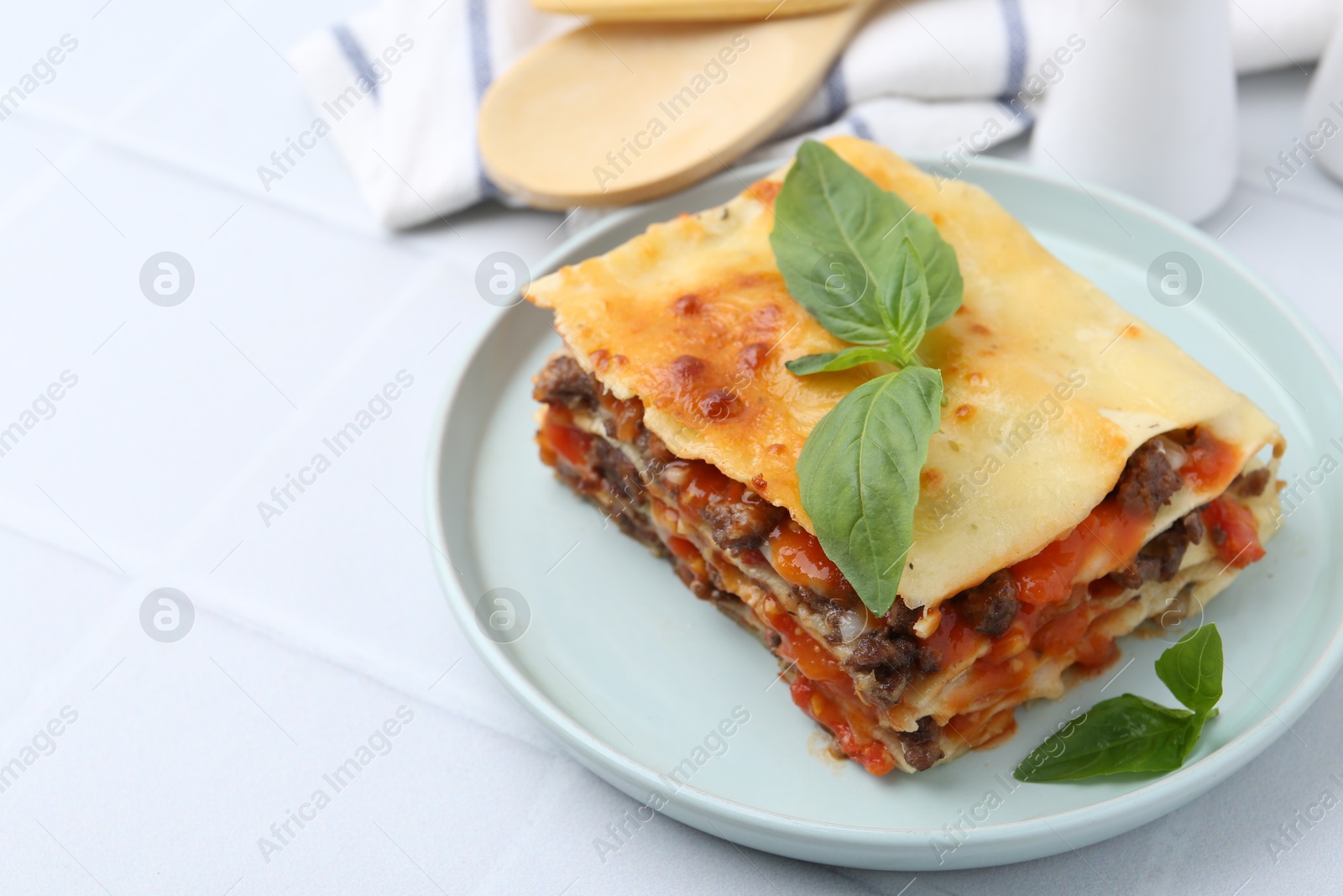 Photo of Delicious cooked lasagna with basil on white tiled table, closeup. Space for text