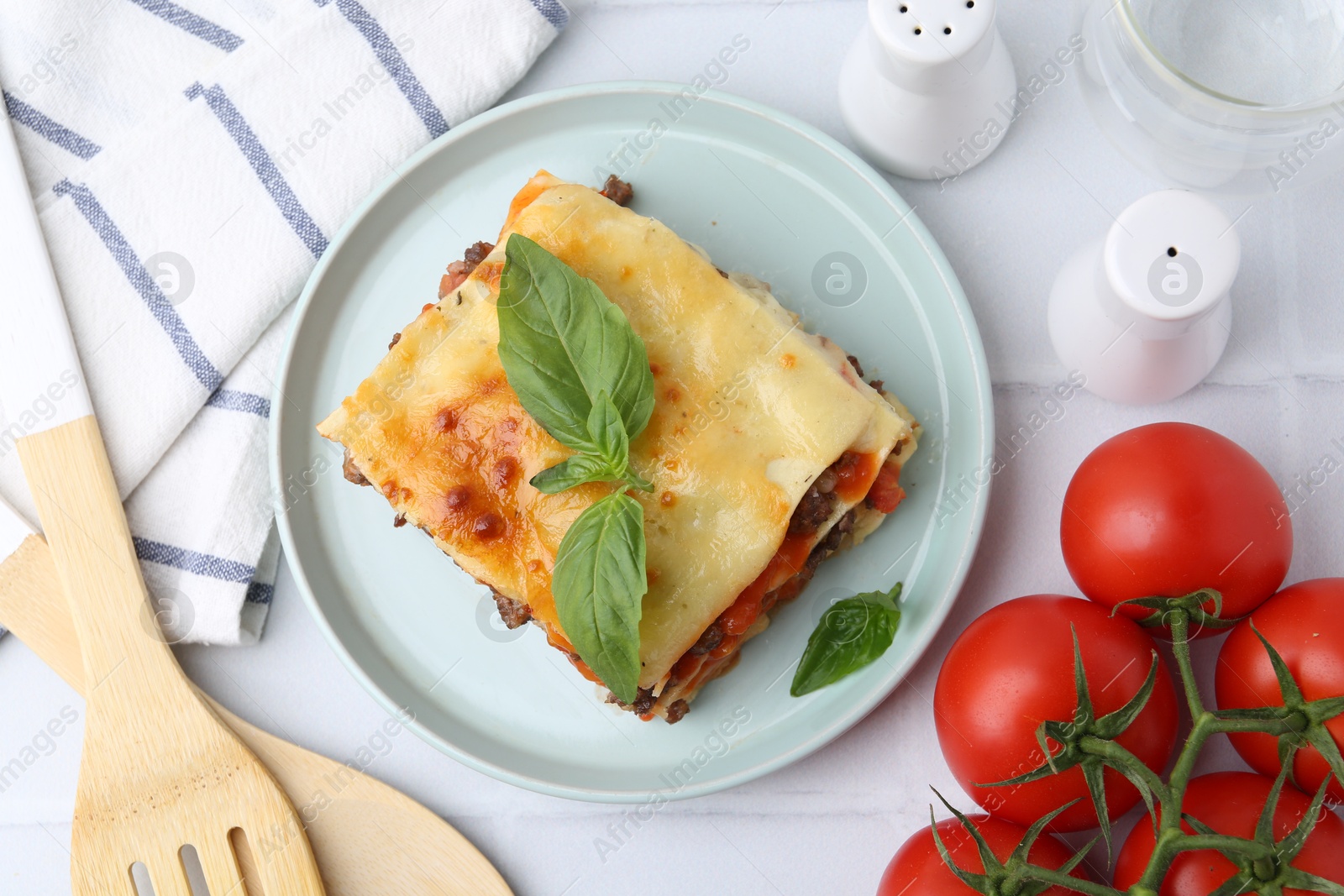 Photo of Delicious cooked lasagna with basil served on white tiled table, flat lay