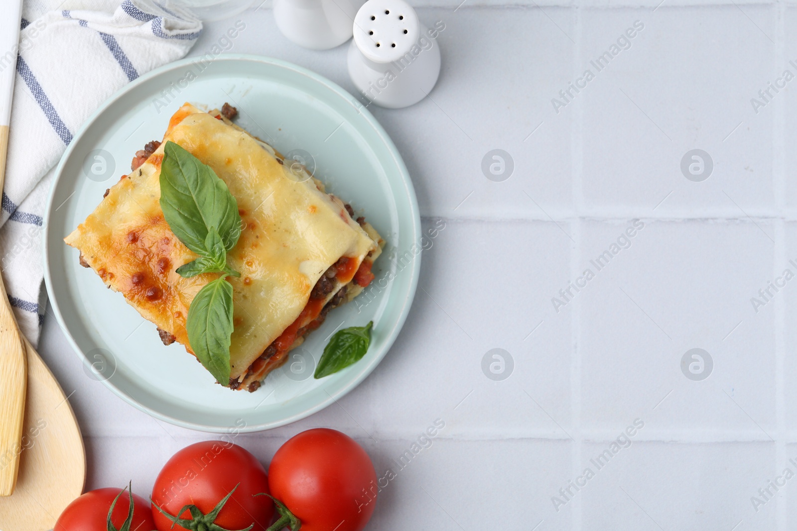 Photo of Delicious cooked lasagna with basil served on white tiled table, flat lay. Space for text