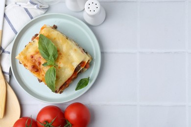 Photo of Delicious cooked lasagna with basil served on white tiled table, flat lay. Space for text