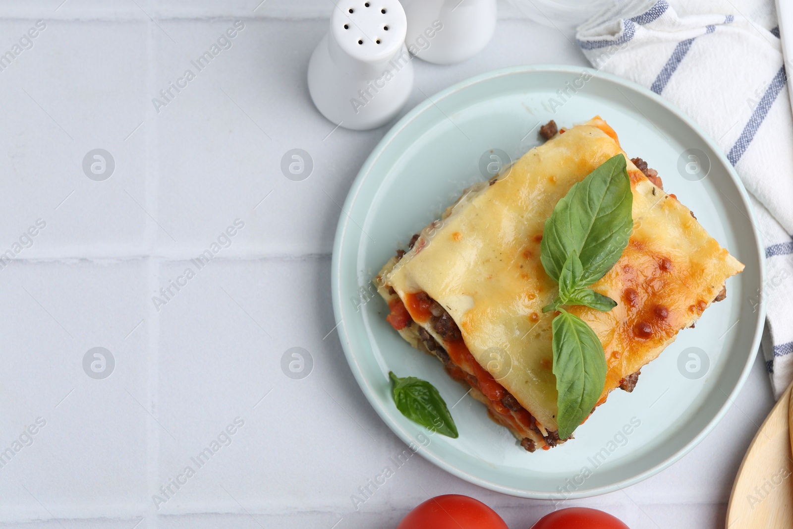 Photo of Delicious cooked lasagna with basil served on white tiled table, flat lay. Space for text