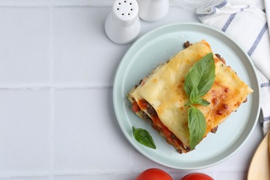 Photo of Delicious cooked lasagna with basil served on white tiled table, flat lay. Space for text