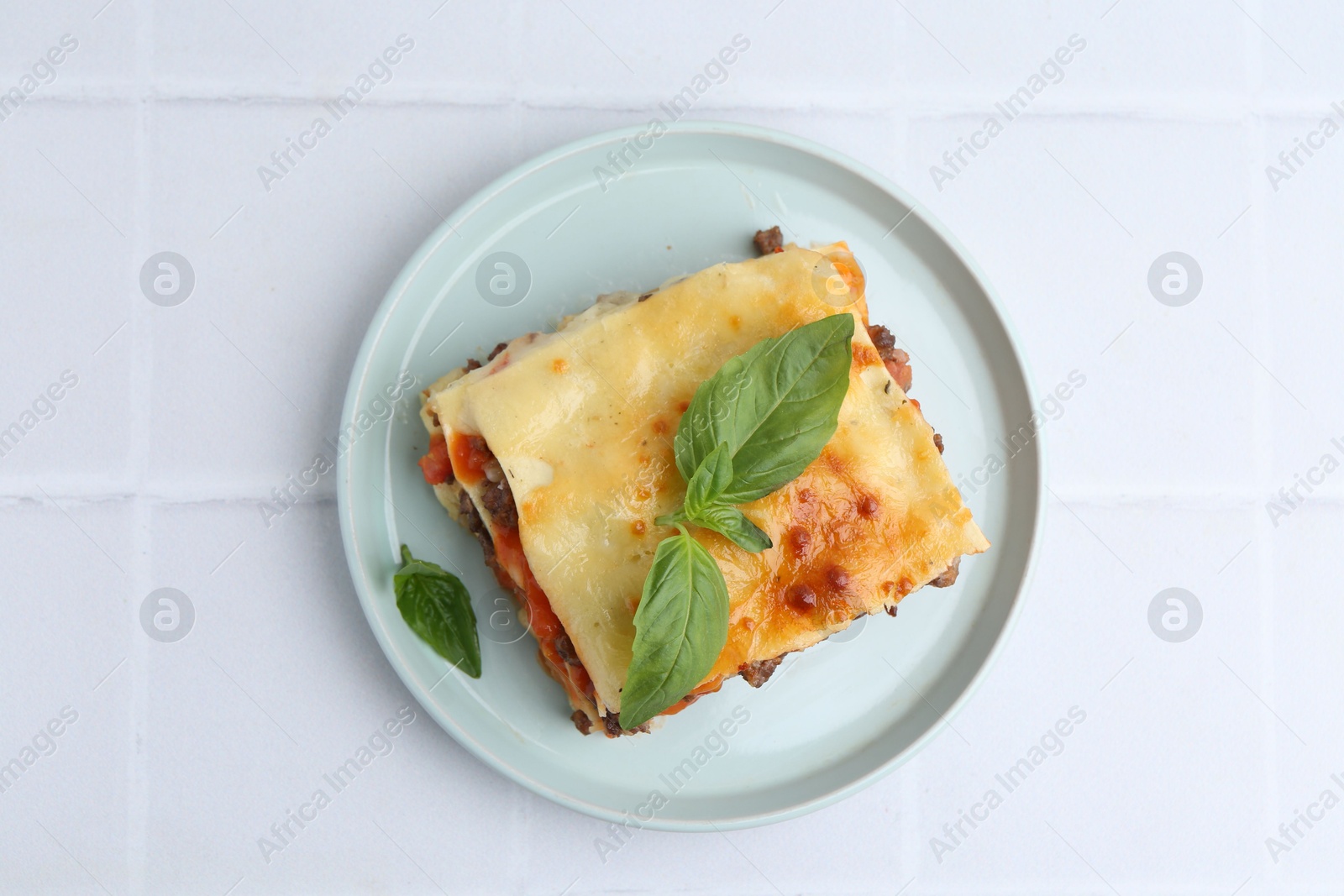 Photo of Delicious cooked lasagna with basil on white tiled table, top view