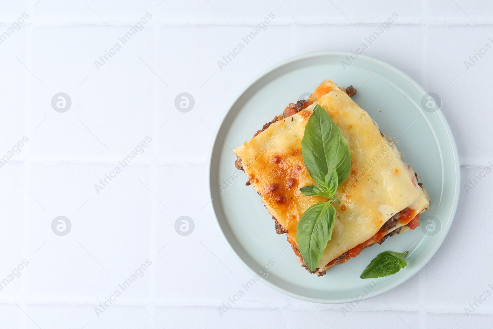 Photo of Delicious cooked lasagna with basil on white tiled table, top view. Space for text