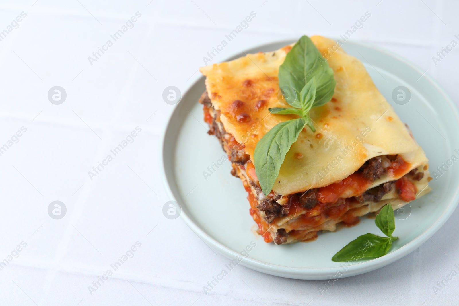 Photo of Delicious cooked lasagna with basil on white tiled table, closeup. Space for text