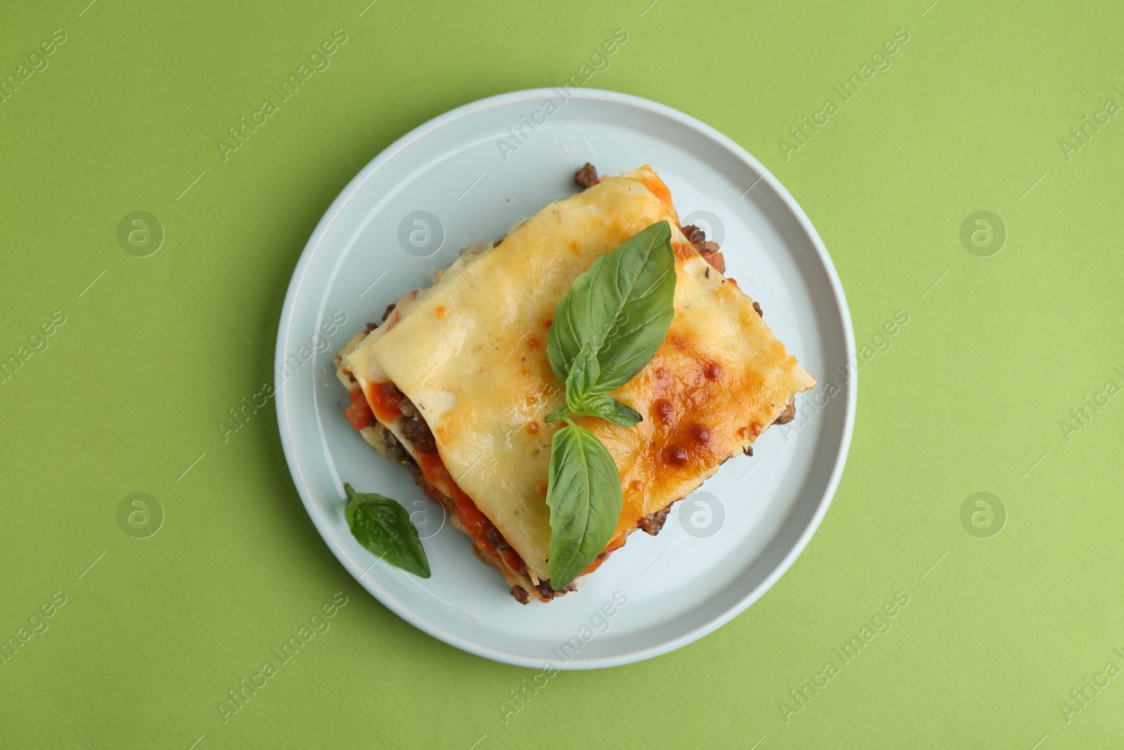 Photo of Delicious cooked lasagna with basil on light green table, top view