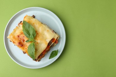 Delicious cooked lasagna with basil on light green table, top view. Space for text