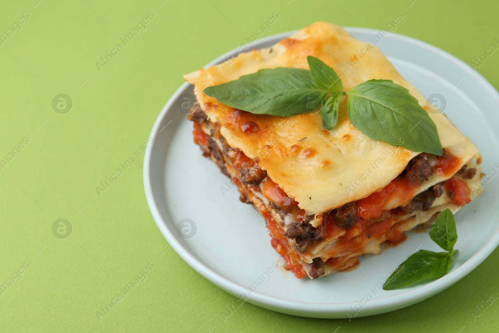 Photo of Delicious cooked lasagna with basil on light green table, closeup. Space for text