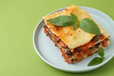 Photo of Delicious cooked lasagna with basil on light green table, closeup. Space for text