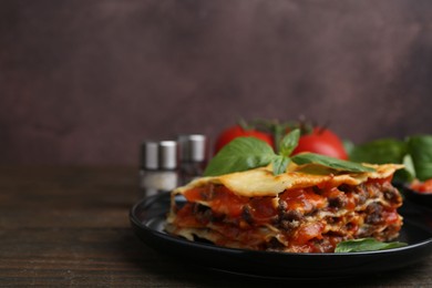 Delicious cooked lasagna with basil on wooden table, closeup. Space for text