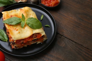 Photo of Delicious cooked lasagna with basil on wooden table, closeup. Space for text