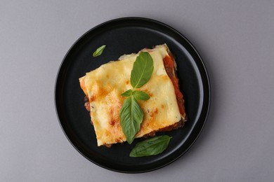 Delicious cooked lasagna with basil on grey table, top view