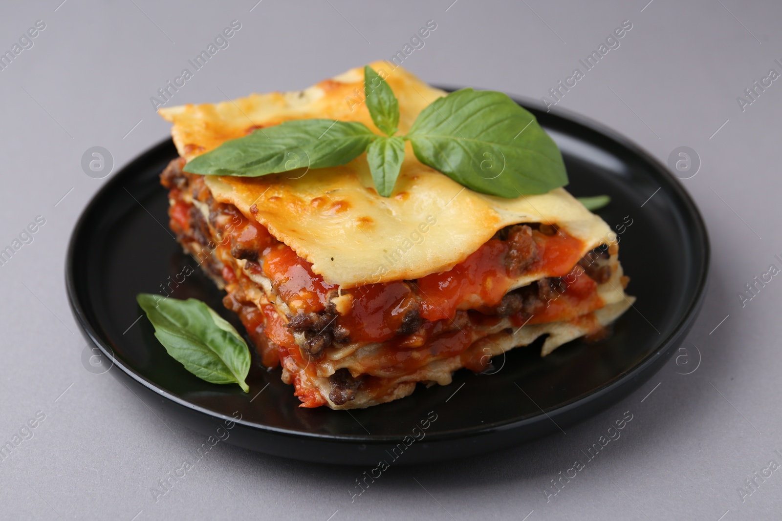 Photo of Delicious cooked lasagna with basil on grey table, closeup