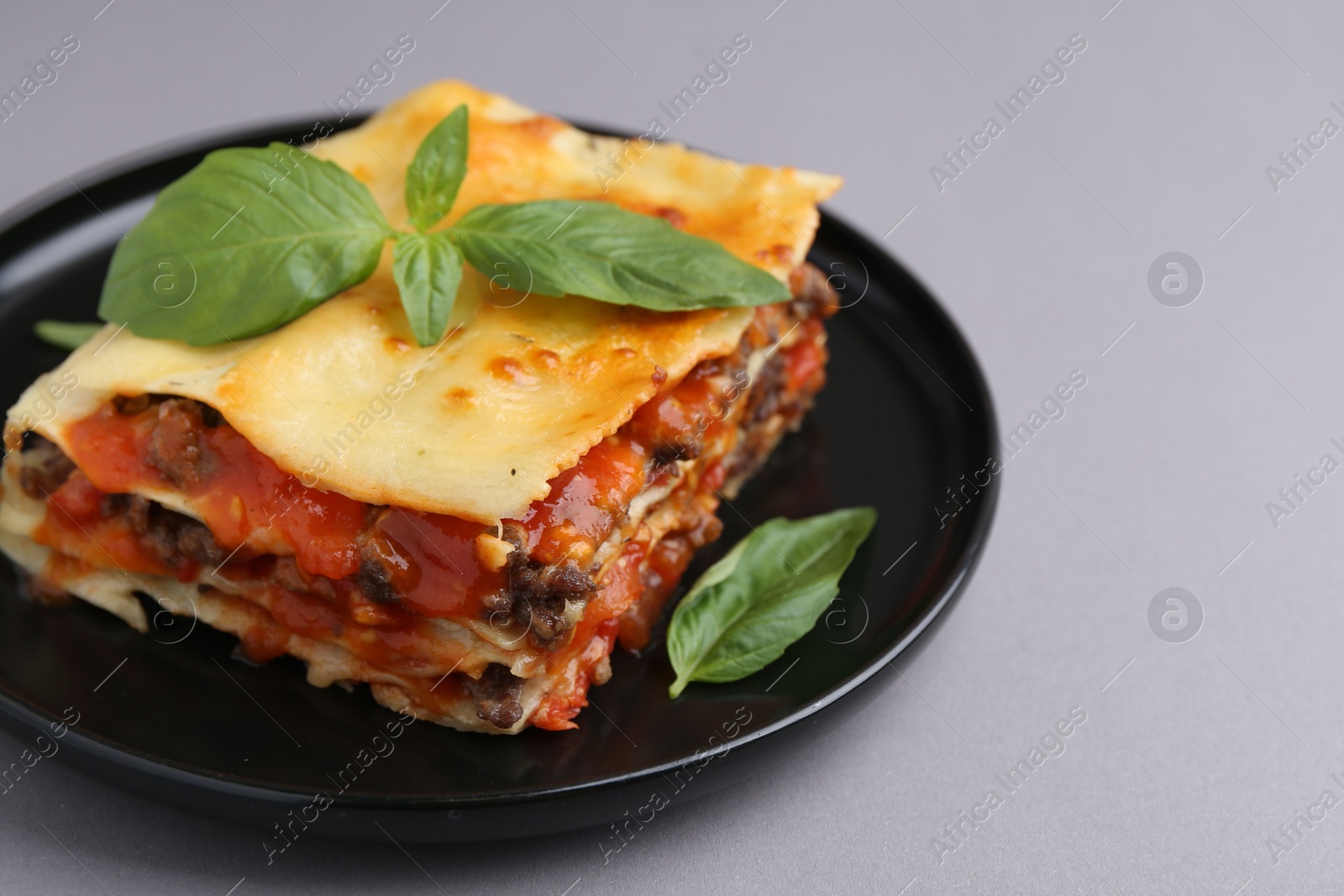 Photo of Delicious cooked lasagna with basil on grey table, closeup. Space for text