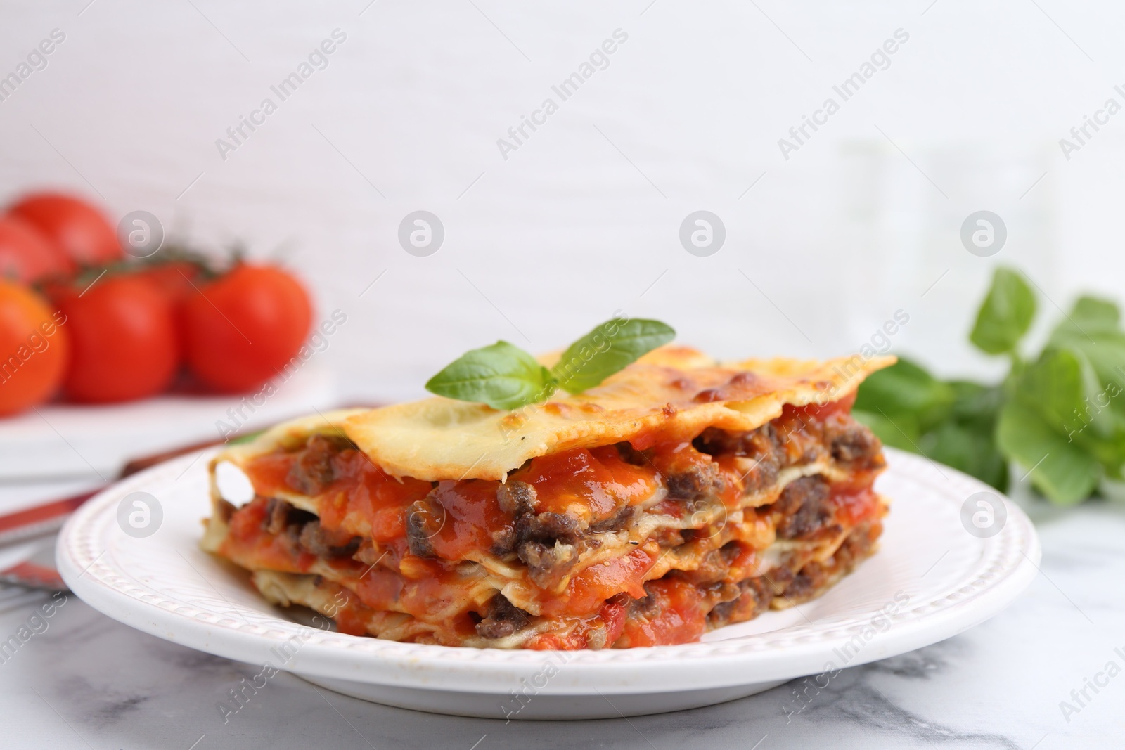 Photo of Delicious cooked lasagna with basil on white marble table, closeup