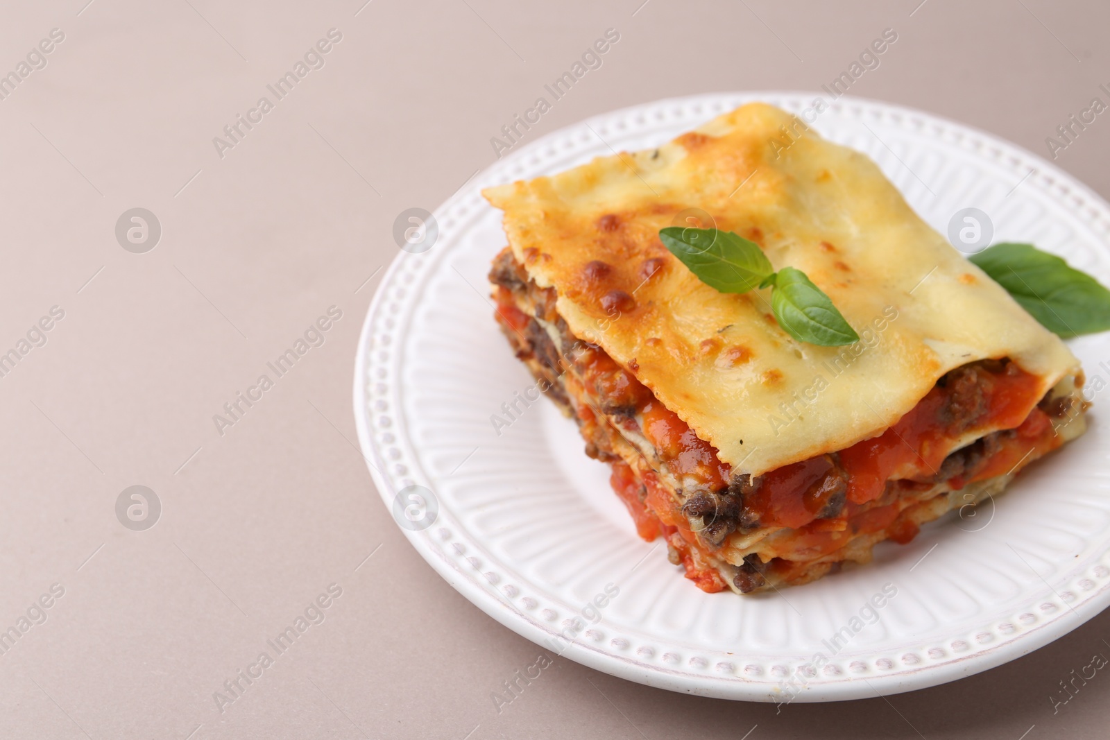 Photo of Delicious cooked lasagna with basil on light grey table, closeup. Space for text