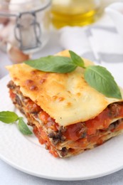 Delicious cooked lasagna with basil on light table, closeup