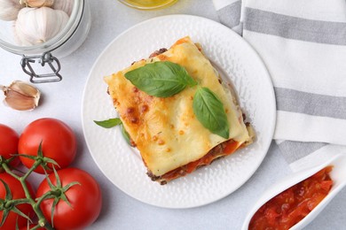 Photo of Delicious cooked lasagna and ingredients on light table, flat lay