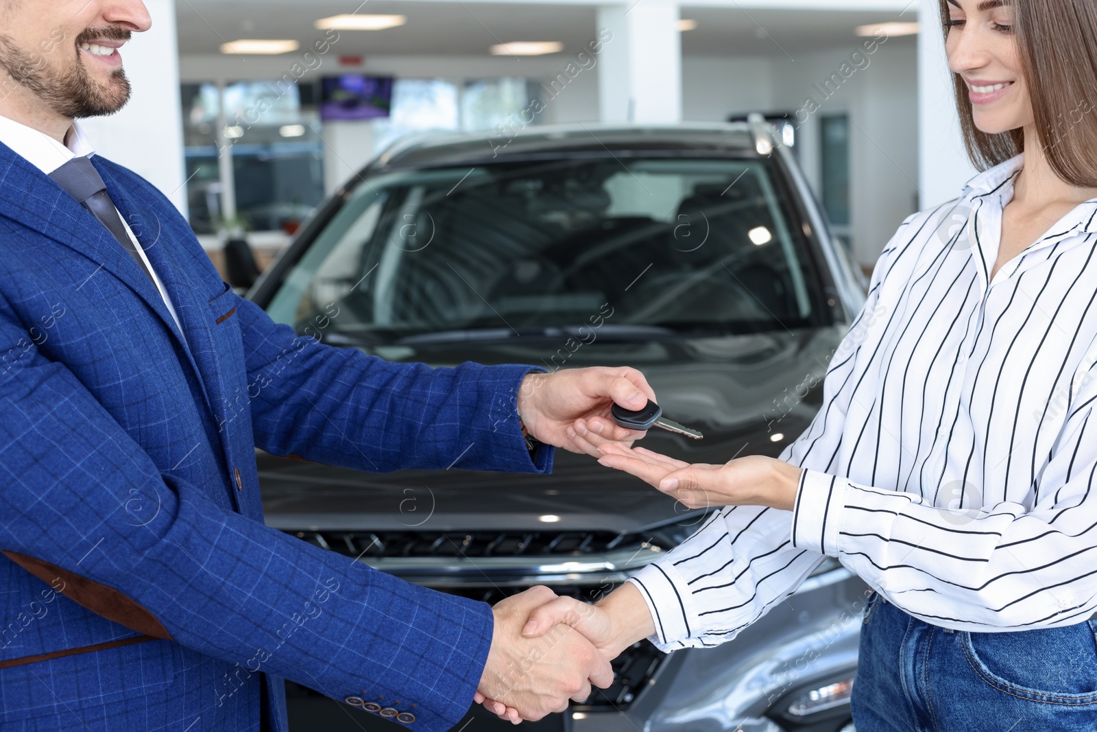 Photo of Salesman giving key to client near new car in salon, closeup