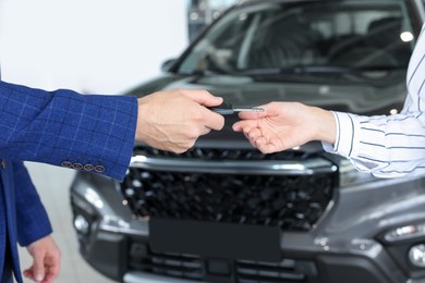 Photo of Salesman giving key to client near new car in salon, closeup