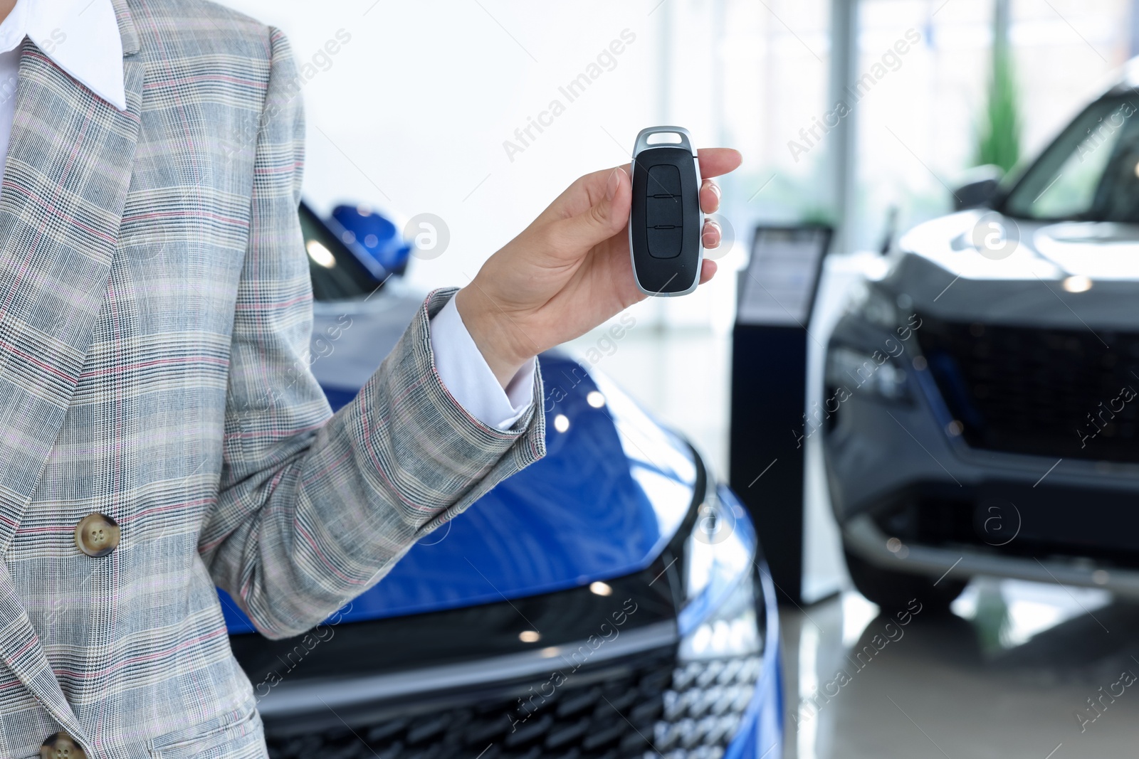 Photo of Saleswoman holding key near new car in salon, closeup