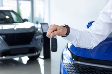 Photo of Salesman holding key near new car in salon, closeup