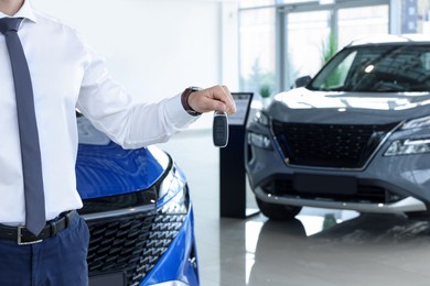 Photo of Salesman holding key near new car in salon, closeup