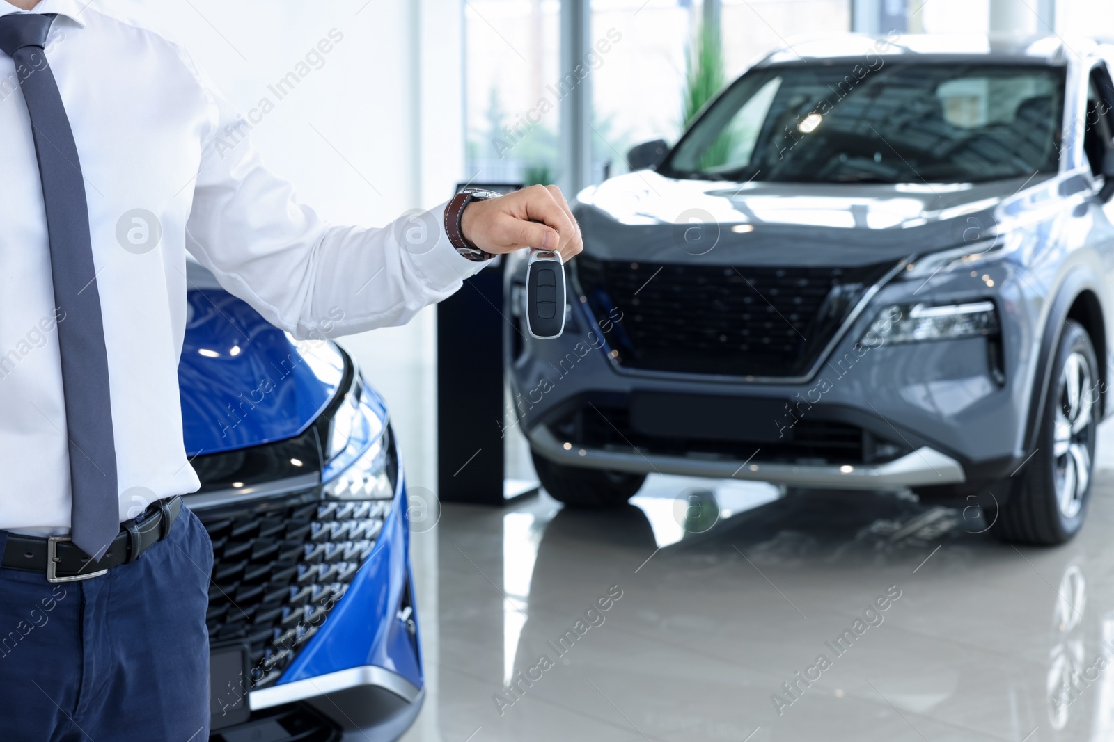 Photo of Salesman holding key near new car in salon, closeup