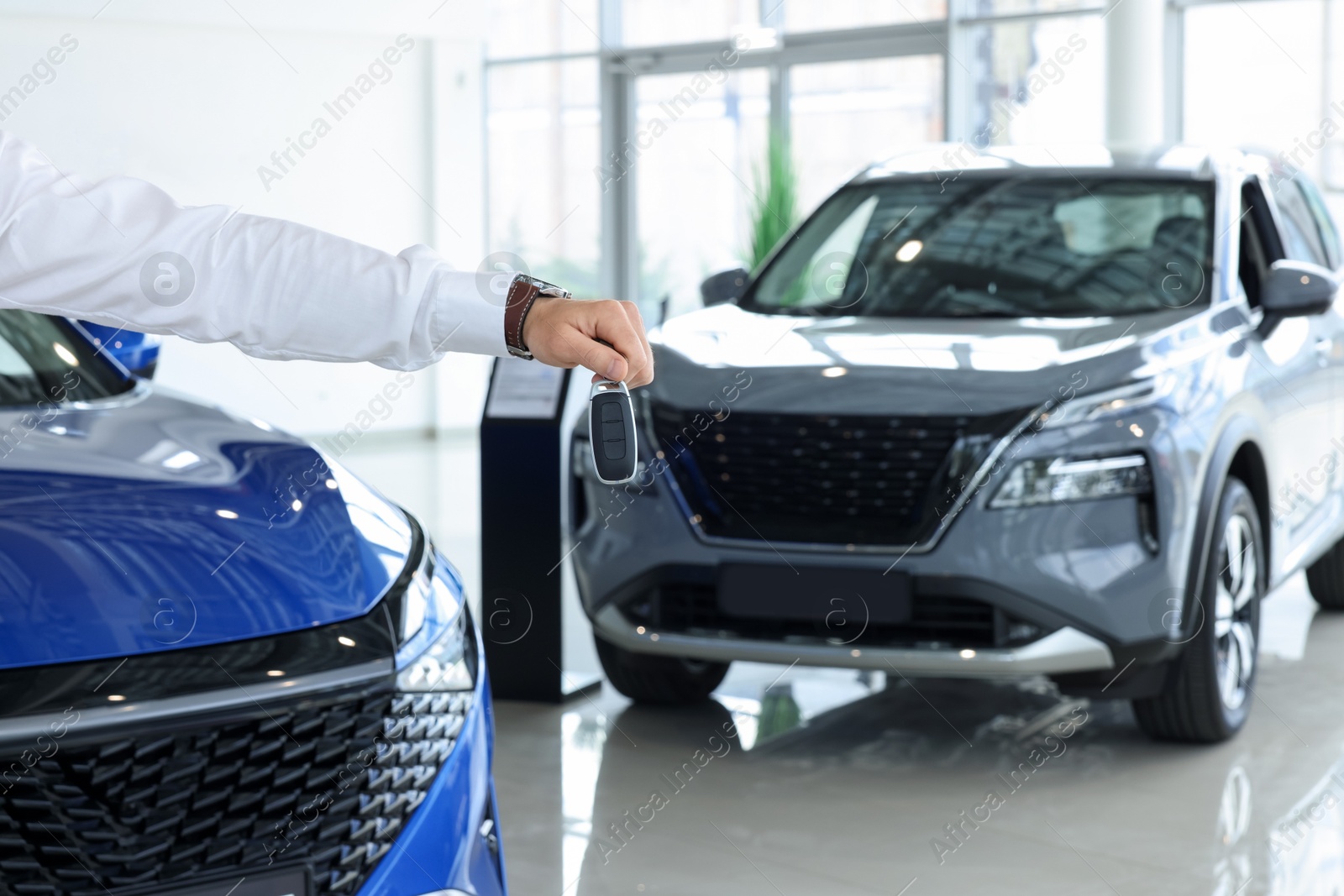 Photo of Salesman holding key near new car in salon, closeup