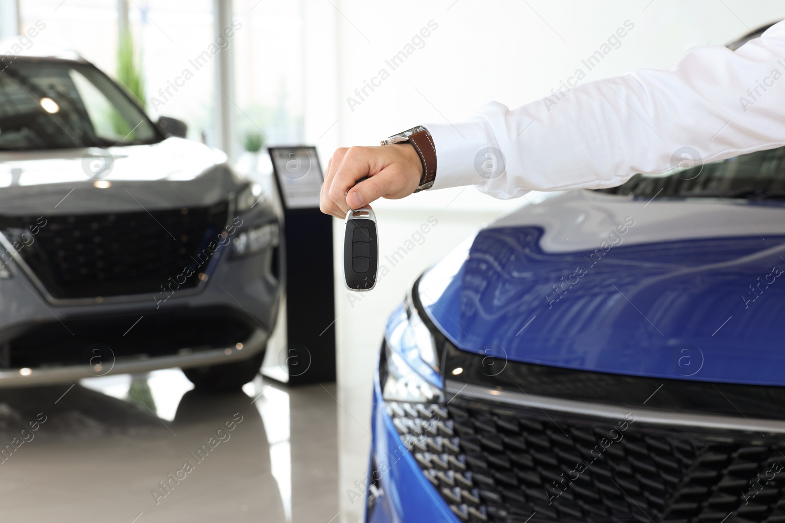 Photo of Salesman holding key near new car in salon, closeup