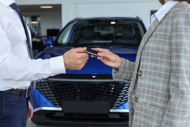 Photo of Saleswoman giving key to client near new car in salon, closeup