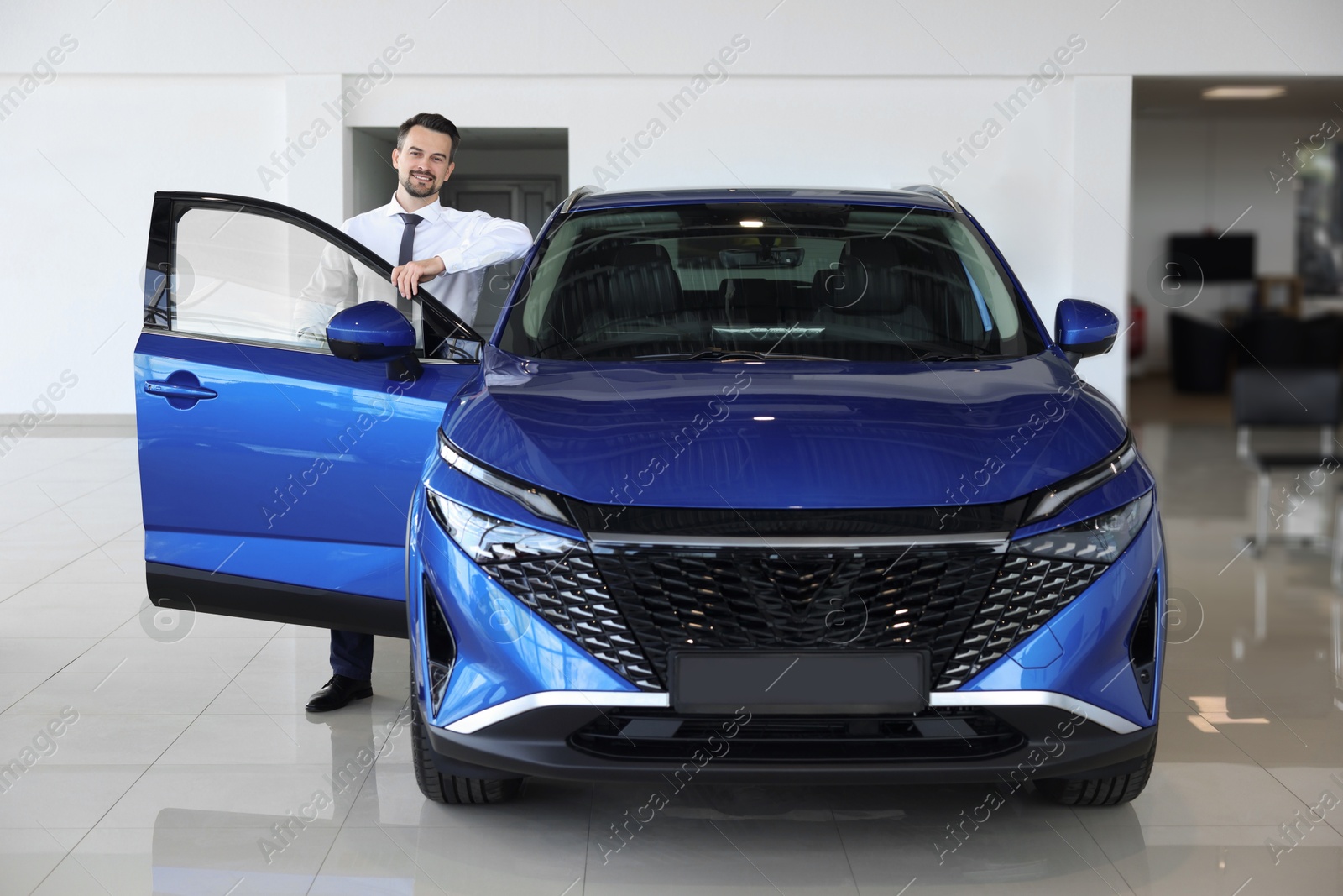 Photo of Happy man near new blue car in salon