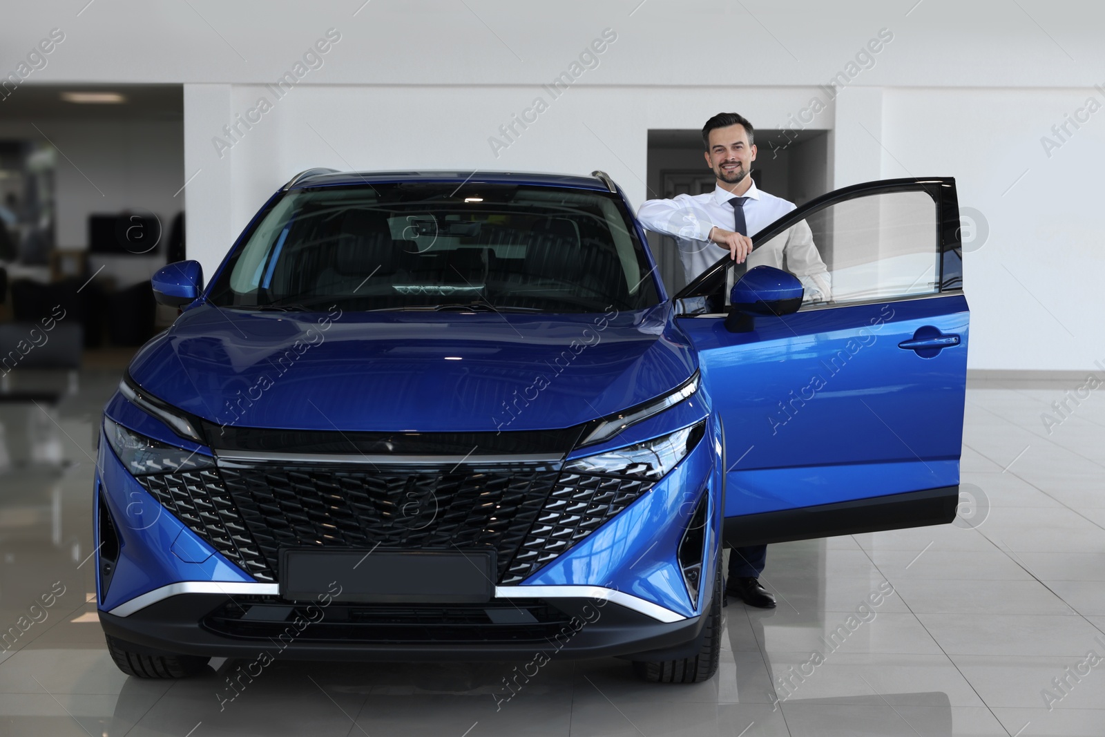 Photo of Happy man near new blue car in salon