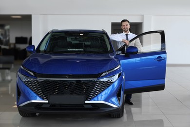 Happy man near new blue car in salon