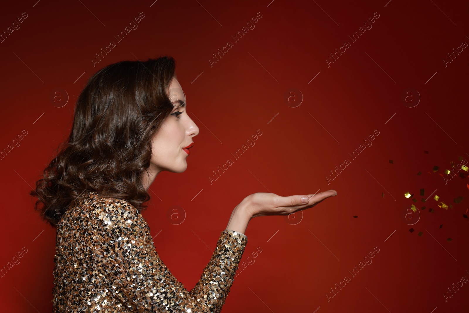 Photo of Woman with perfect makeup blowing confetti on red background. Space for text