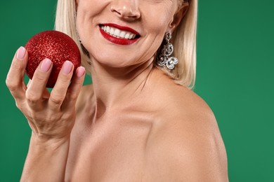 Photo of Smiling woman with Christmas bauble on green background, closeup