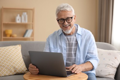 Photo of Senior man using laptop at wooden table indoors