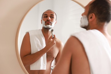 Photo of Handsome man applying shaving foam near mirror in bathroom