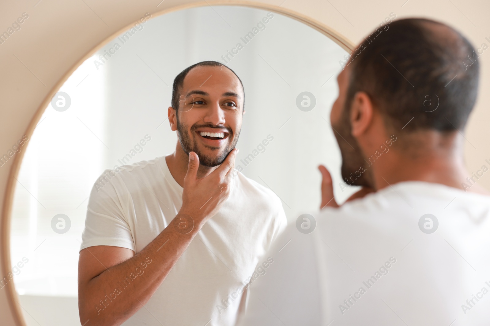 Photo of Smiling man looking at mirror in bathroom