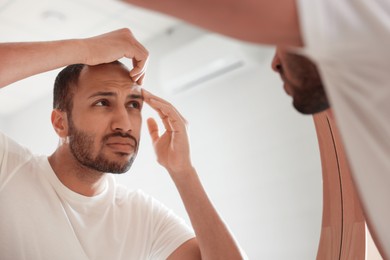 Photo of Worried man looking at mirror in bathroom