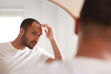 Photo of Worried man looking at mirror in bathroom