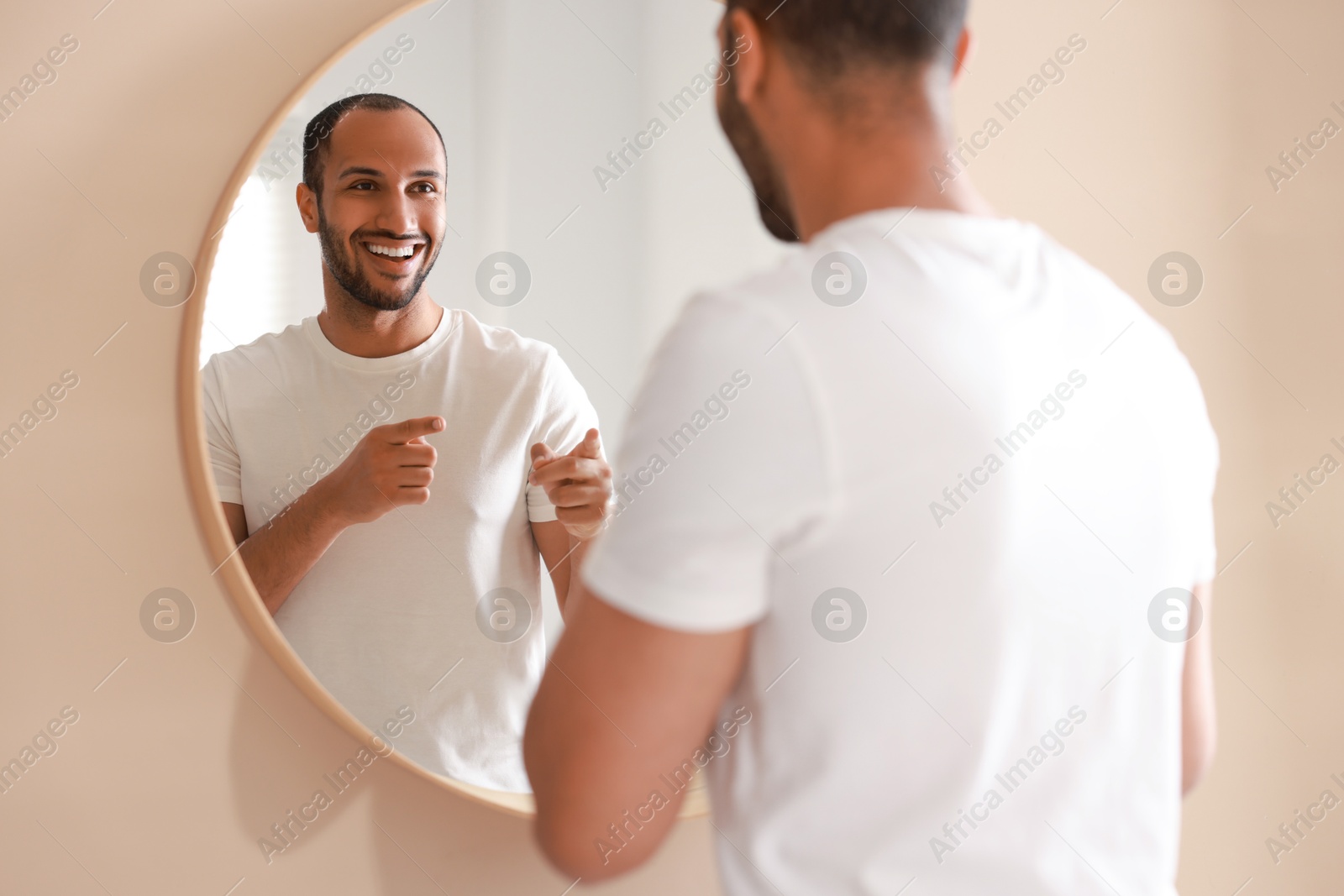 Photo of Smiling man looking at mirror in bathroom, back view